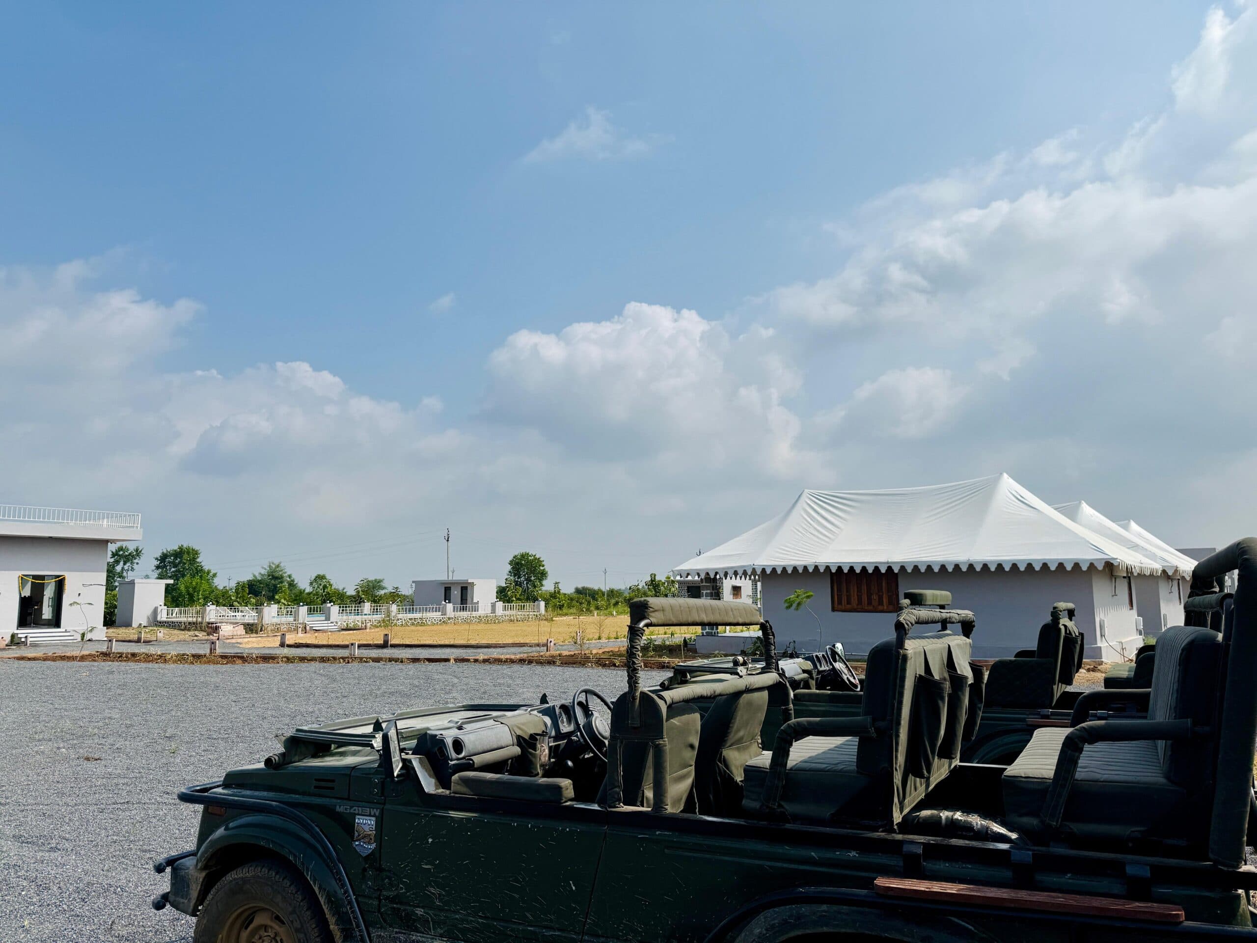 An open safari jeep waiting on the drive at Upvan Jawai, tented cottages behind it